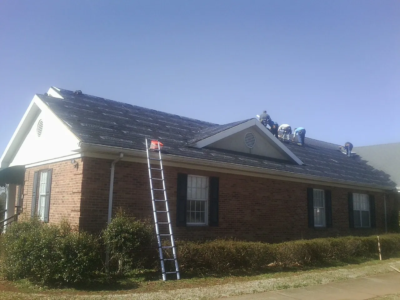 Crew tearing shingles off a brick ranch roof with a ladder set — Emergency Roof Repair work by our crew in Mooresburg