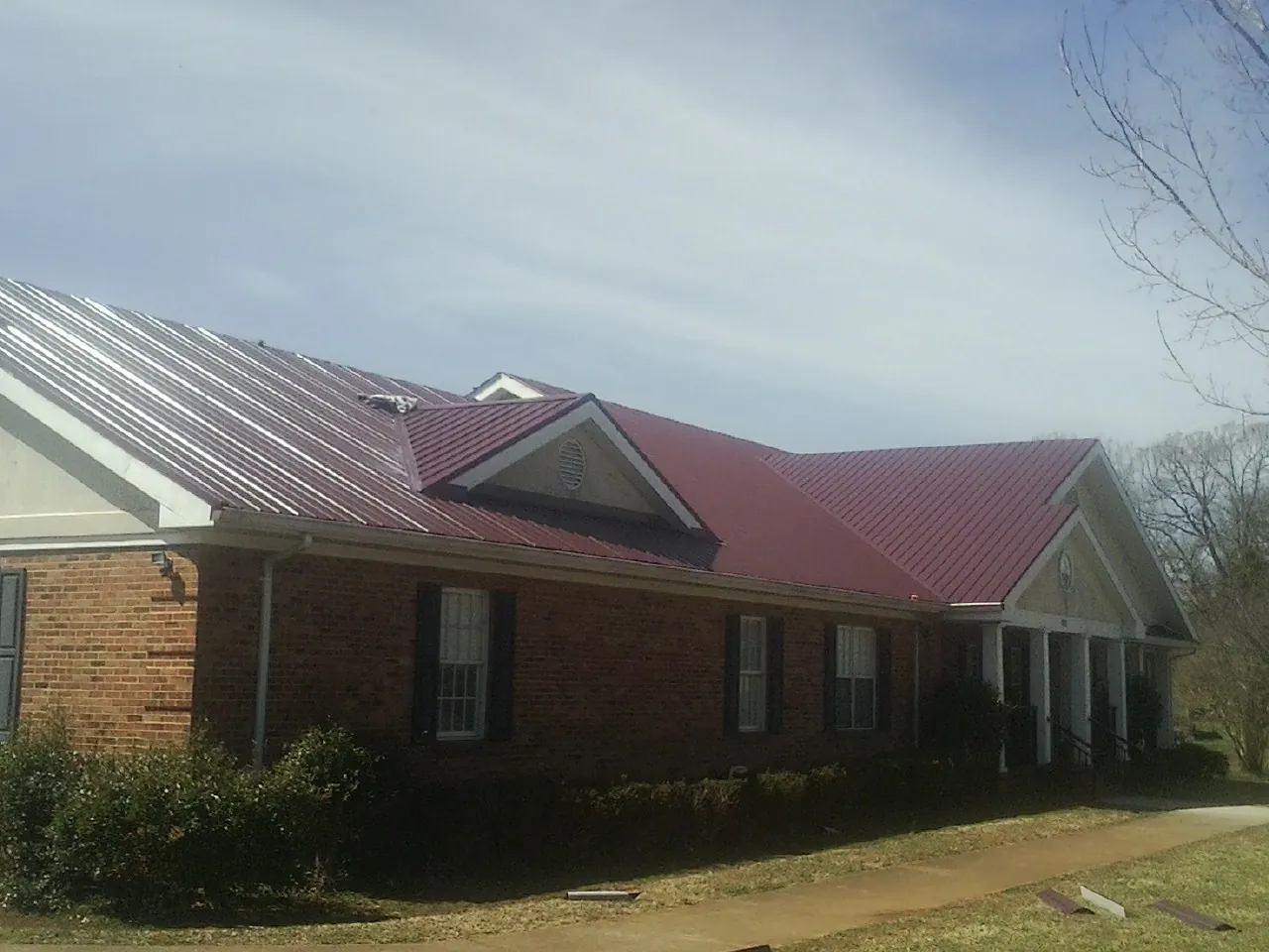 Red metal roof with gabled entries on a long brick building, from a Hail Damage Roof Repair job in Mooresburg