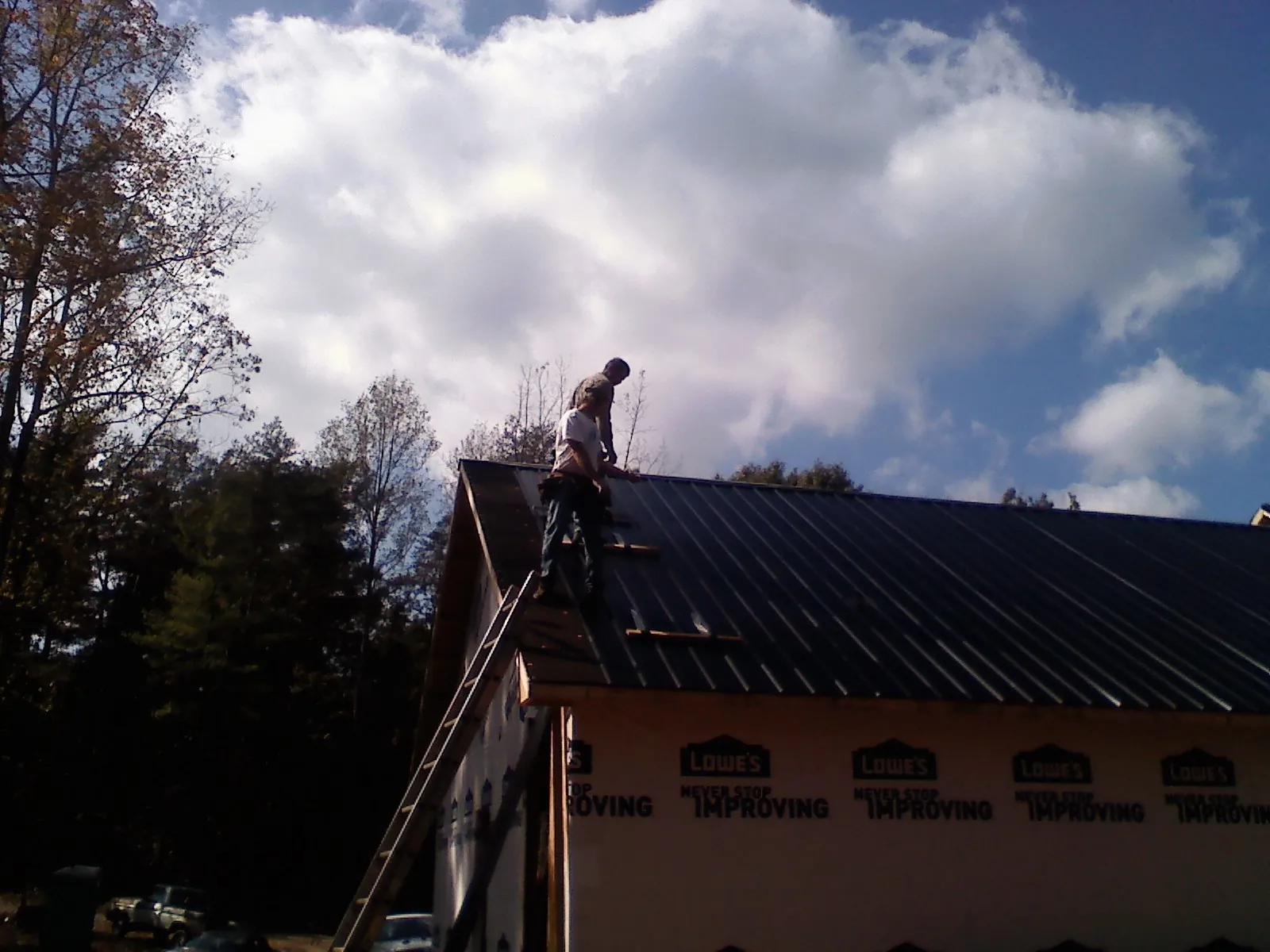 Roofer fastening dark metal panels high against a cloudy sky, from a Roof Inspection job in Mooresburg