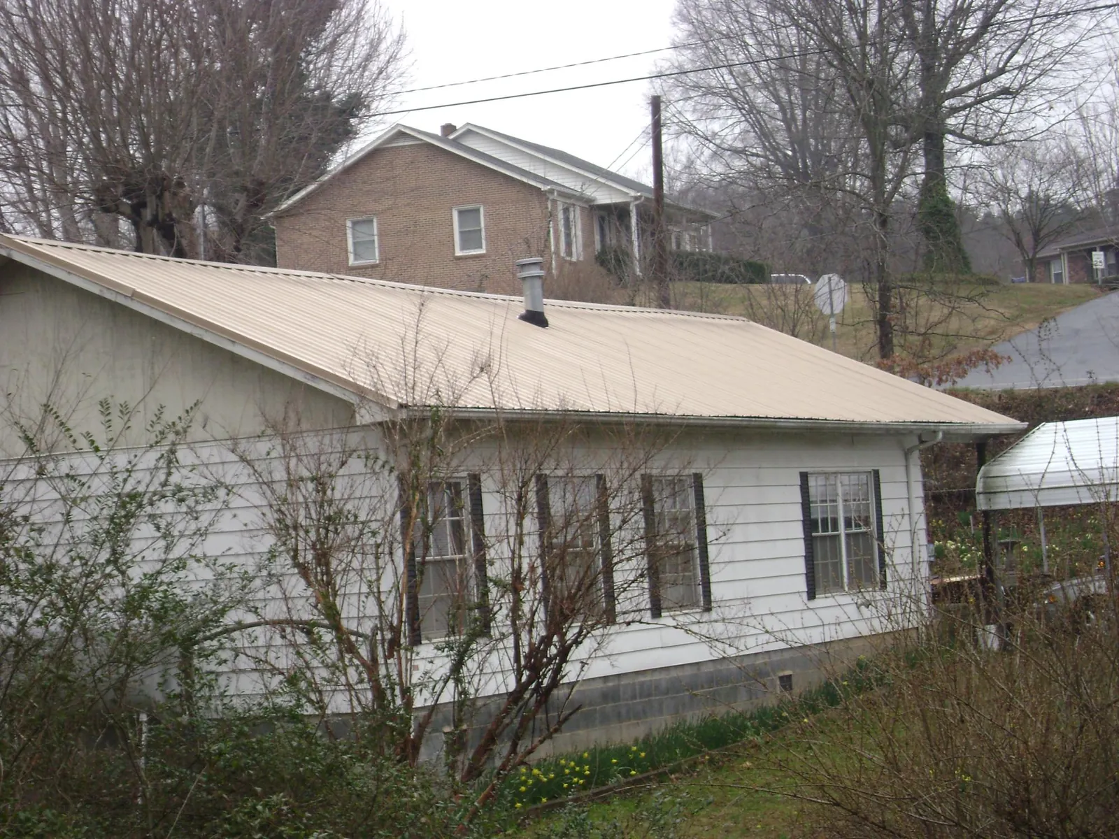 Tan metal roof on a white sided house set into a hillside — Commercial Roofing by Roofing Brothers in Mooresburg